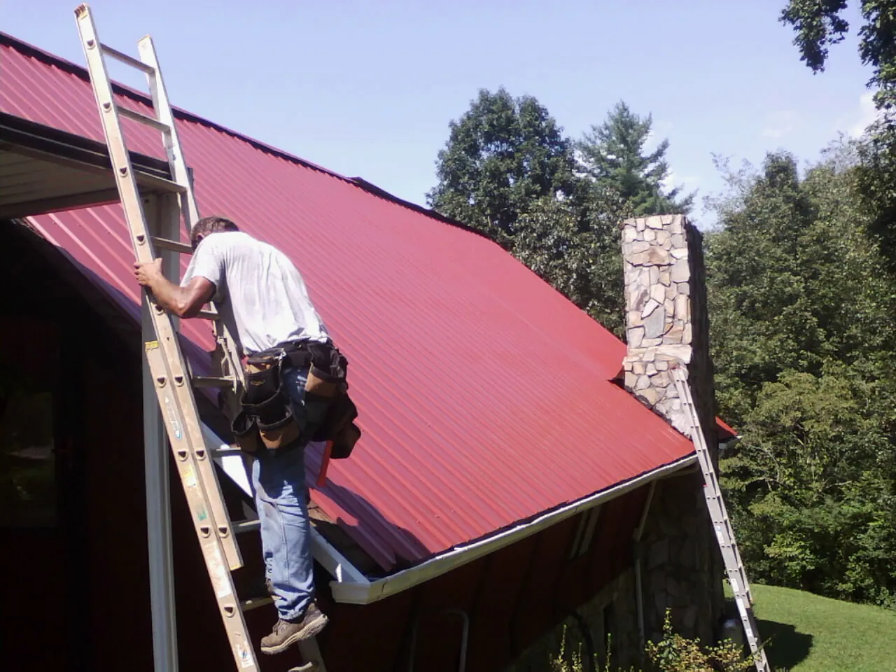Roofer on a ladder beside a red metal roof and stone chimney in Lexington