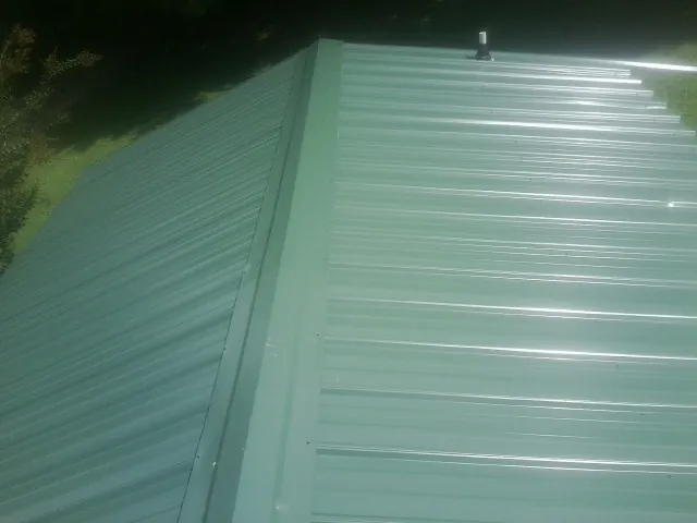 New green metal panels meeting at the ridge of a roof — Flat Roof Repair work by our crew in Lexington